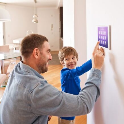 Father teaching son how to use touch screen alarm system in kitchen wall