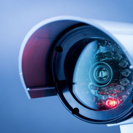 Close up of surveillance camera with light on with blue background